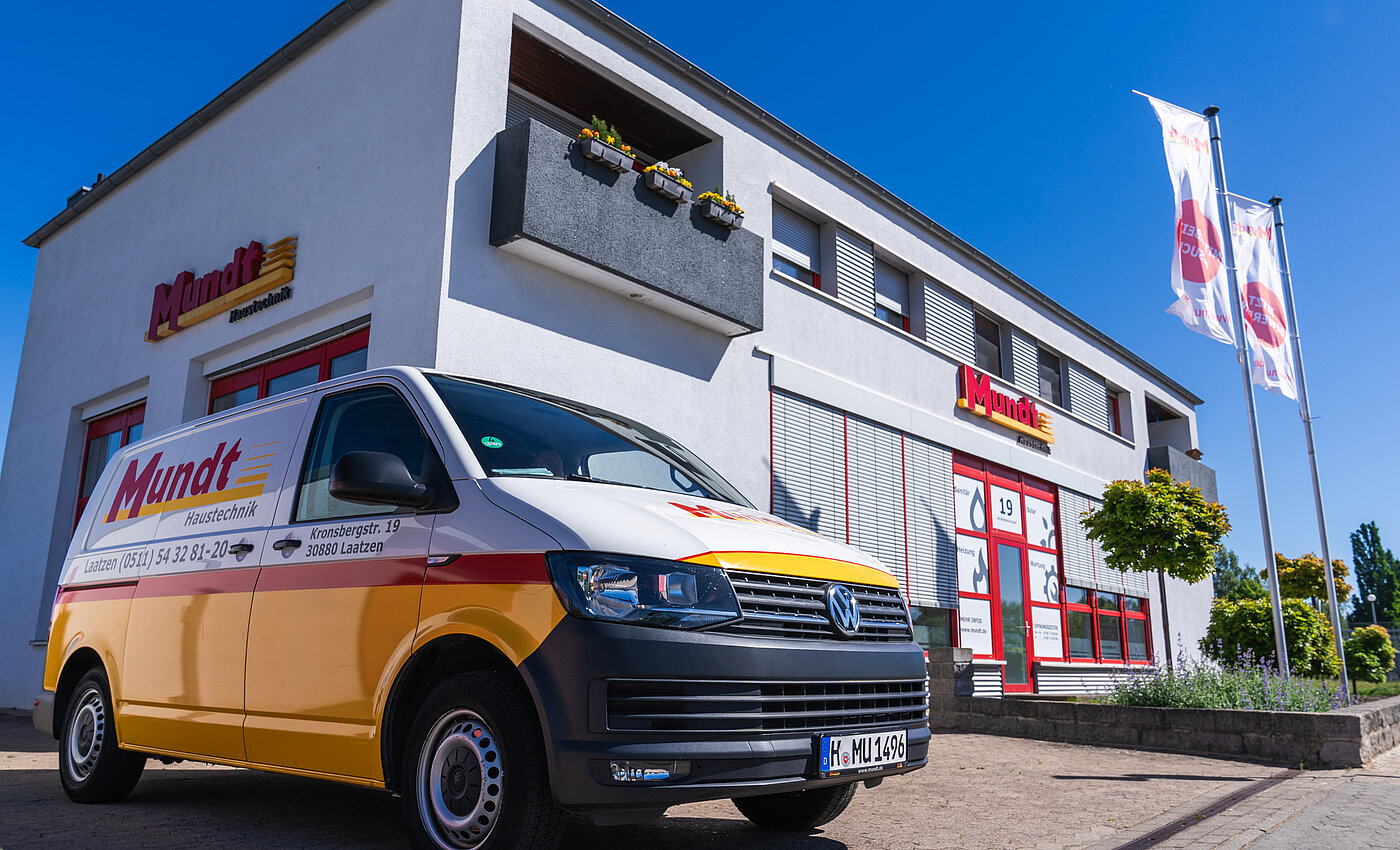 Ein gelber Mundt Haustechnik-Van steht vor einem hellen Firmengebäude mit markanter Schrift und Flaggen.