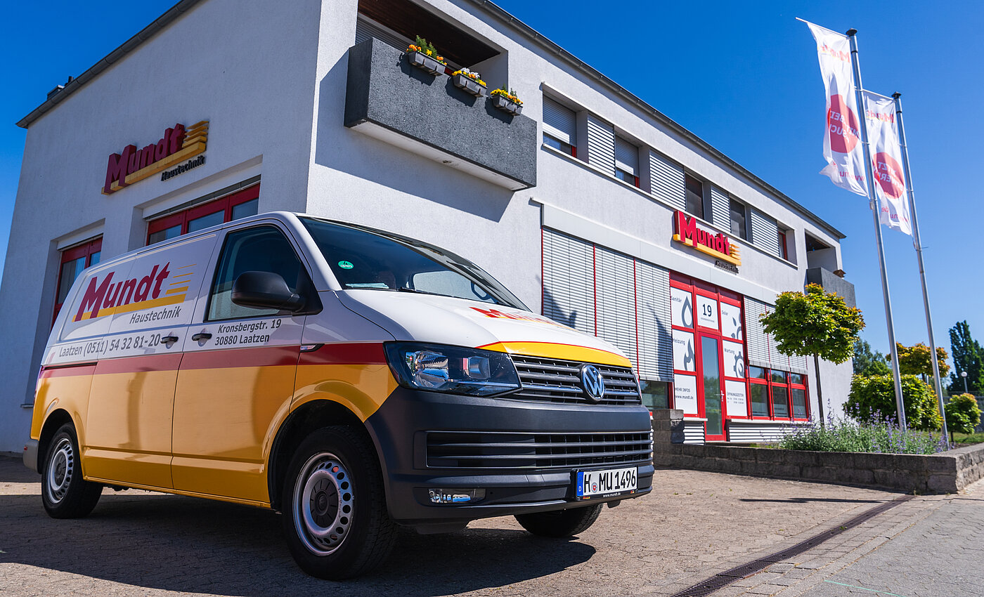 Ein gelber Mundt Haustechnik-Van steht vor einem hellen Firmengebäude mit markanter Schrift und Flaggen.