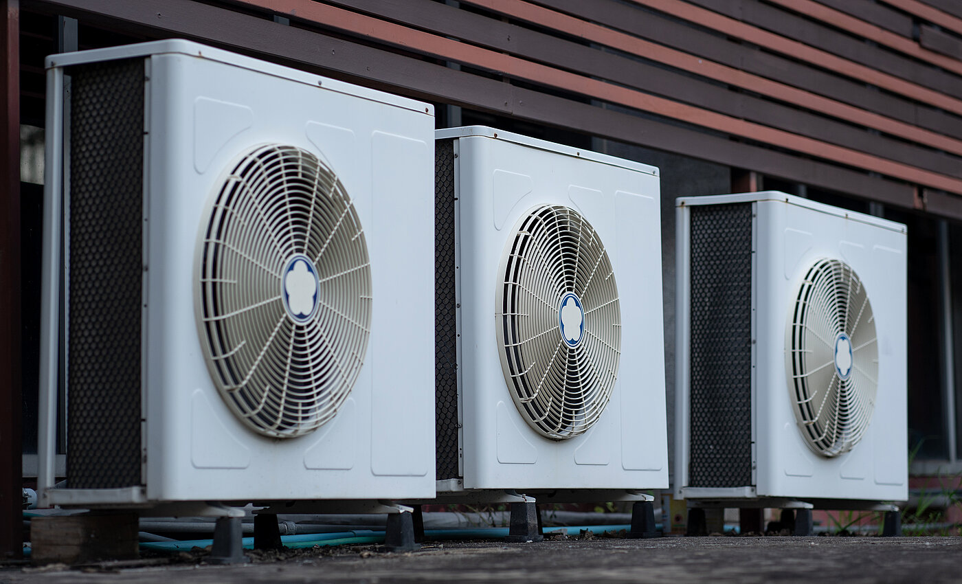 Drei moderne Klimapumpen mit sichtbaren Lüftern vor einem Gebäude installiert.