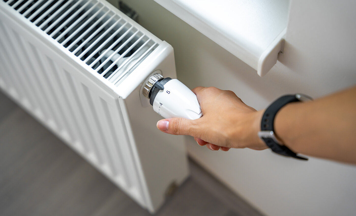 Eine Hand dreht den Thermostat an einem weißen Heizkörper auf die Stufe fünf.
